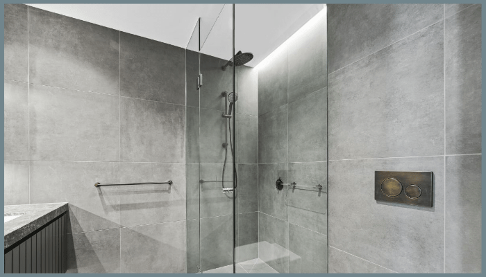 frameless glass shower screen installed in a modern grey-tiled bathroom