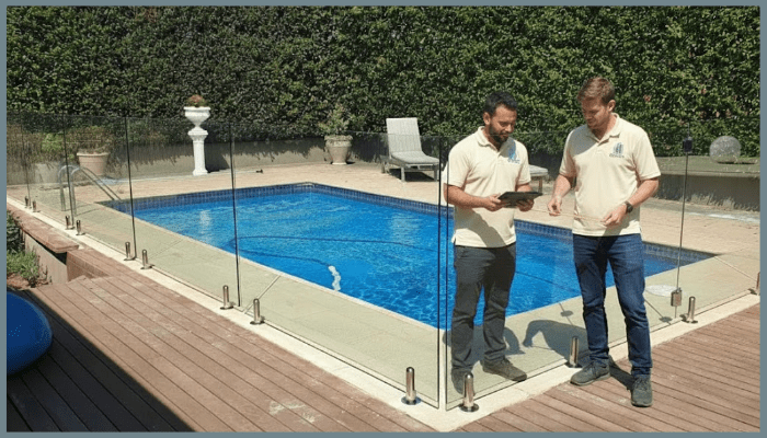 Two inspectors checking pool fence height and compliance in a Canberra backyard, ensuring the glass barrier meets ACT safety standards under AS 1926.1.