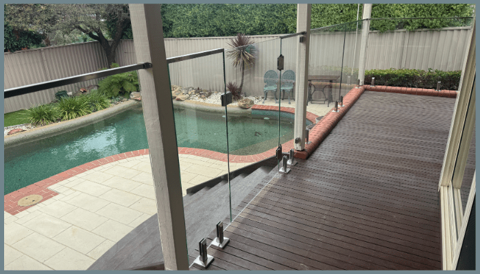 Standoff glass balustrade installed on a timber deck overlooking a backyard pool showing side-mounted fittings and clear glass panels