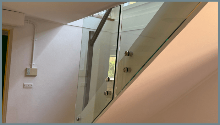 Close-up view of a toughened glass balustrade with 316 stainless steel standoffs installed along an indoor staircase in Canberra.