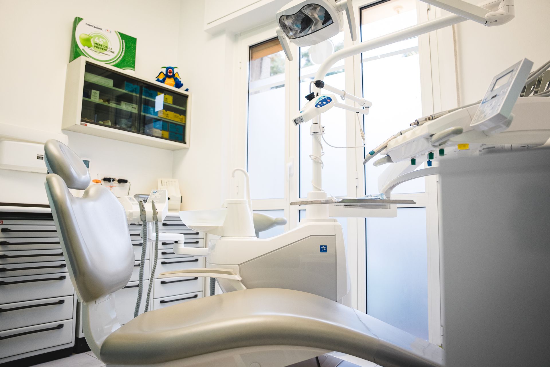 Studio dentistico moderno con pareti bianche, poltrona odontoiatrica grigia e attrezzatura.