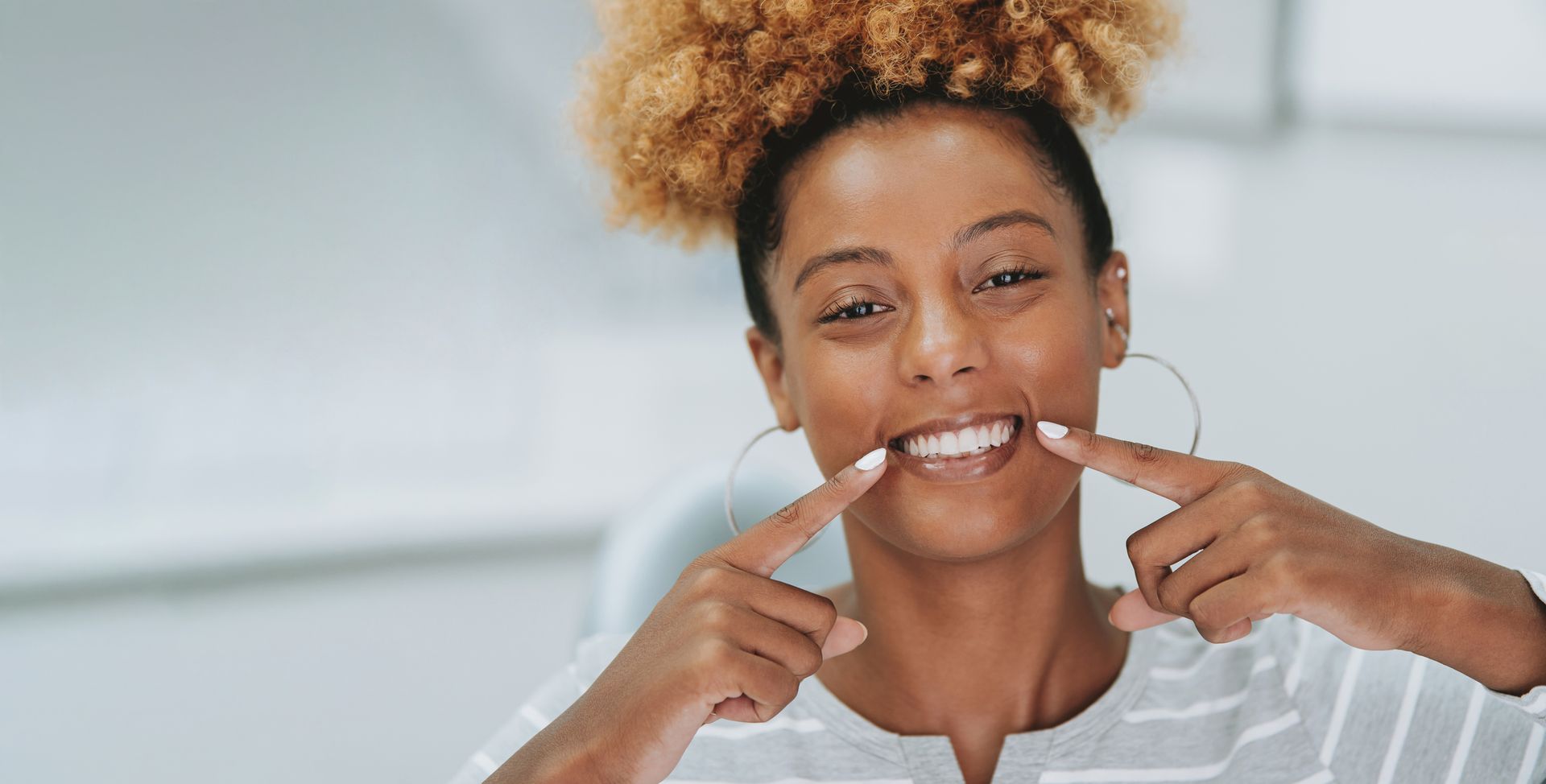 Un dentista esamina i denti di una donna sorridente; si trovano in uno studio medico ed entrambi indossano dispositivi di protezione.