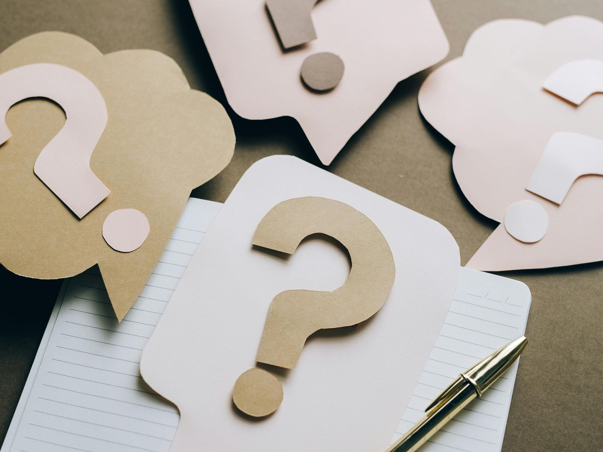 Question mark cutouts on speech bubble shapes and notebook, with a pen.