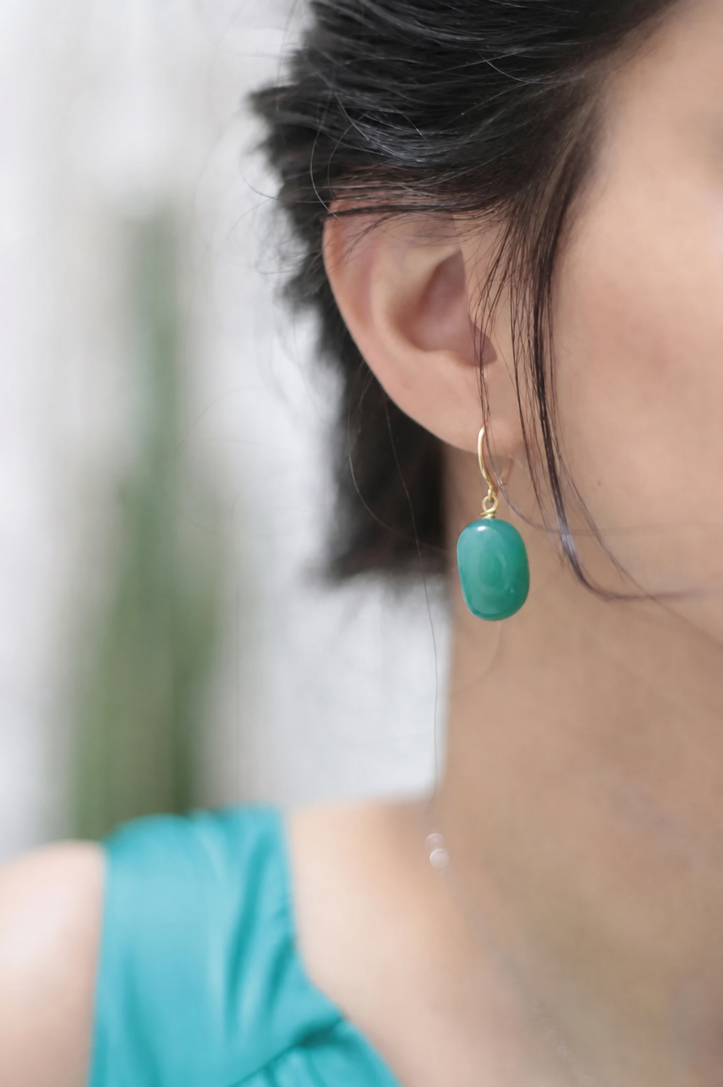 Close-up of a woman’s ear wearing a gold hook earring with a turquoise pendant