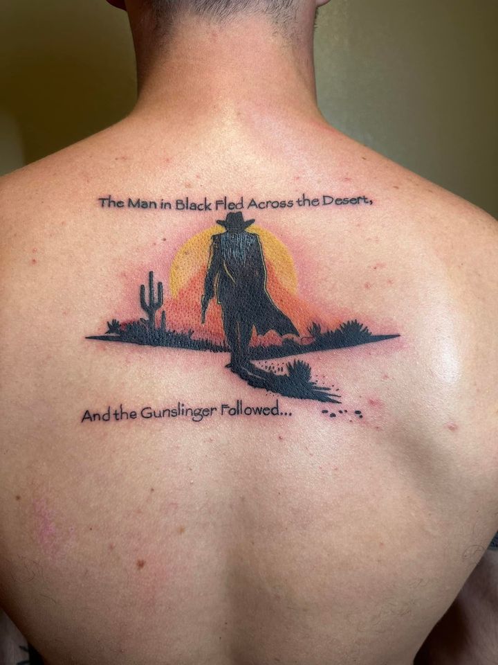Back tattoo with a sunset silhouette of a person and dog, plus small text above and below.