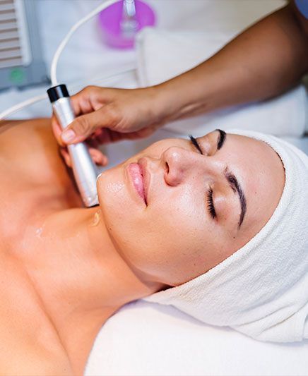Woman receiving a facial treatment with a handheld skincare device in a spa setting