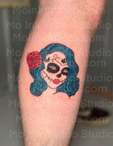 Colorful skull tattoo with teal hair and red rose on a forearm