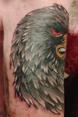 Close-up of a black and gray bird tattoo with a red eye and yellow beak on skin