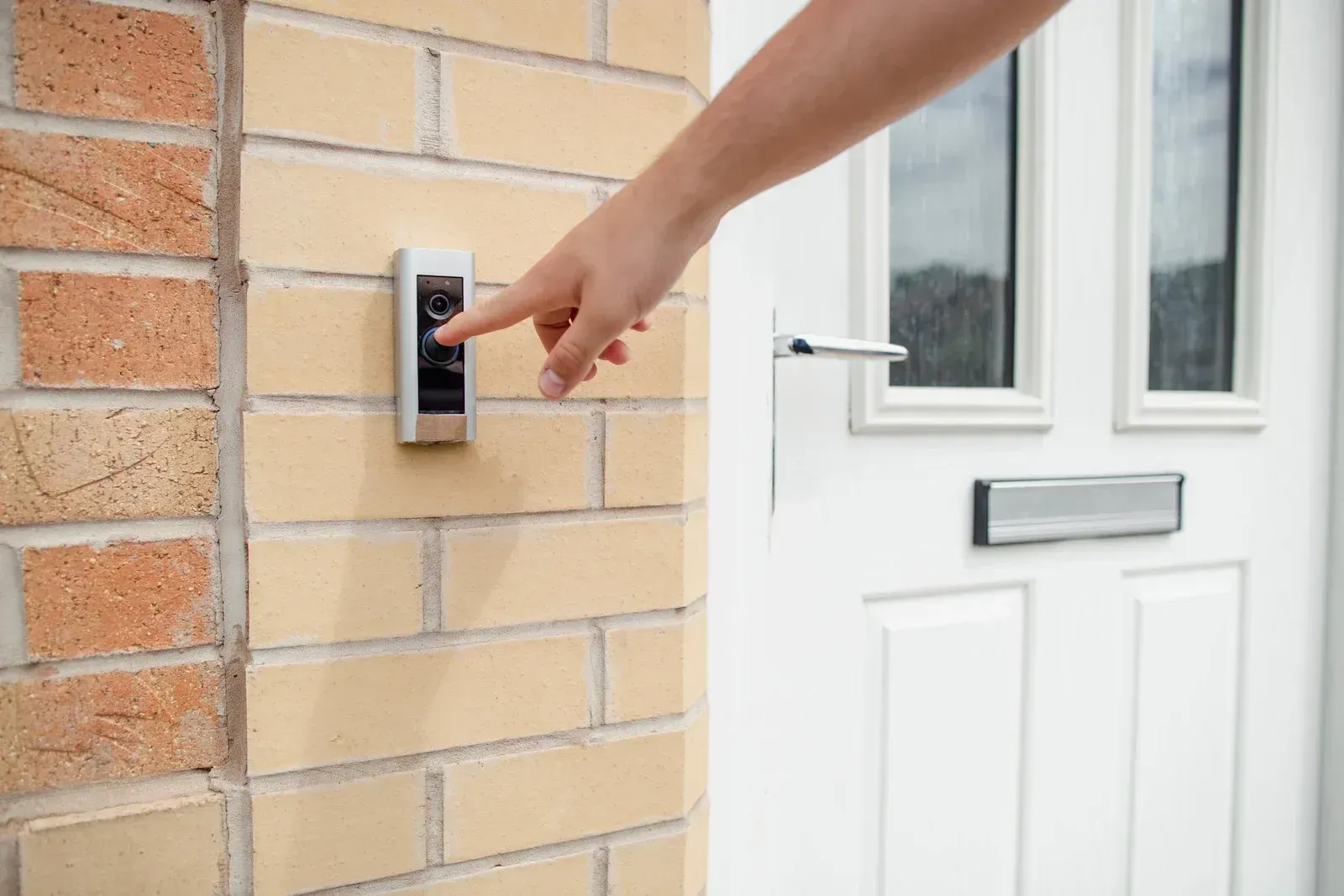A person is pressing a doorbell on a brick wall.