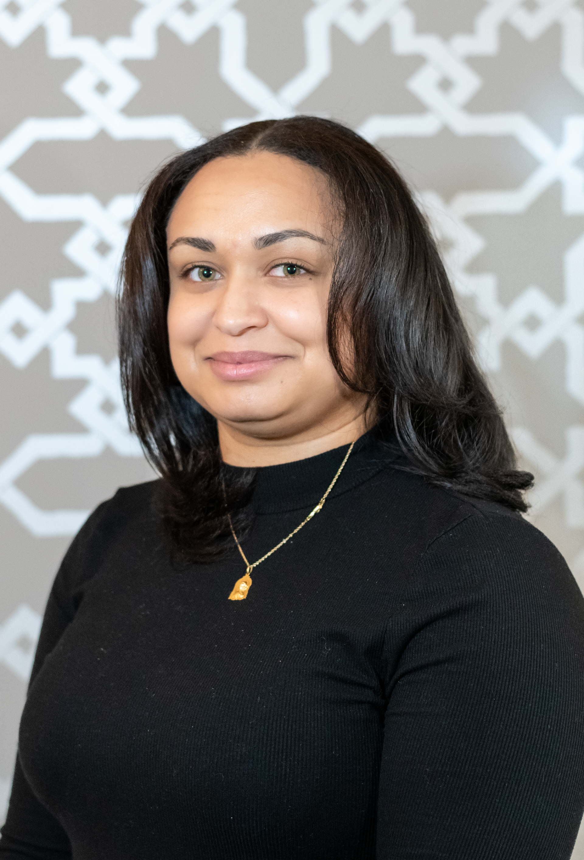 A woman wearing a black sweater and a gold necklace is smiling for the camera.