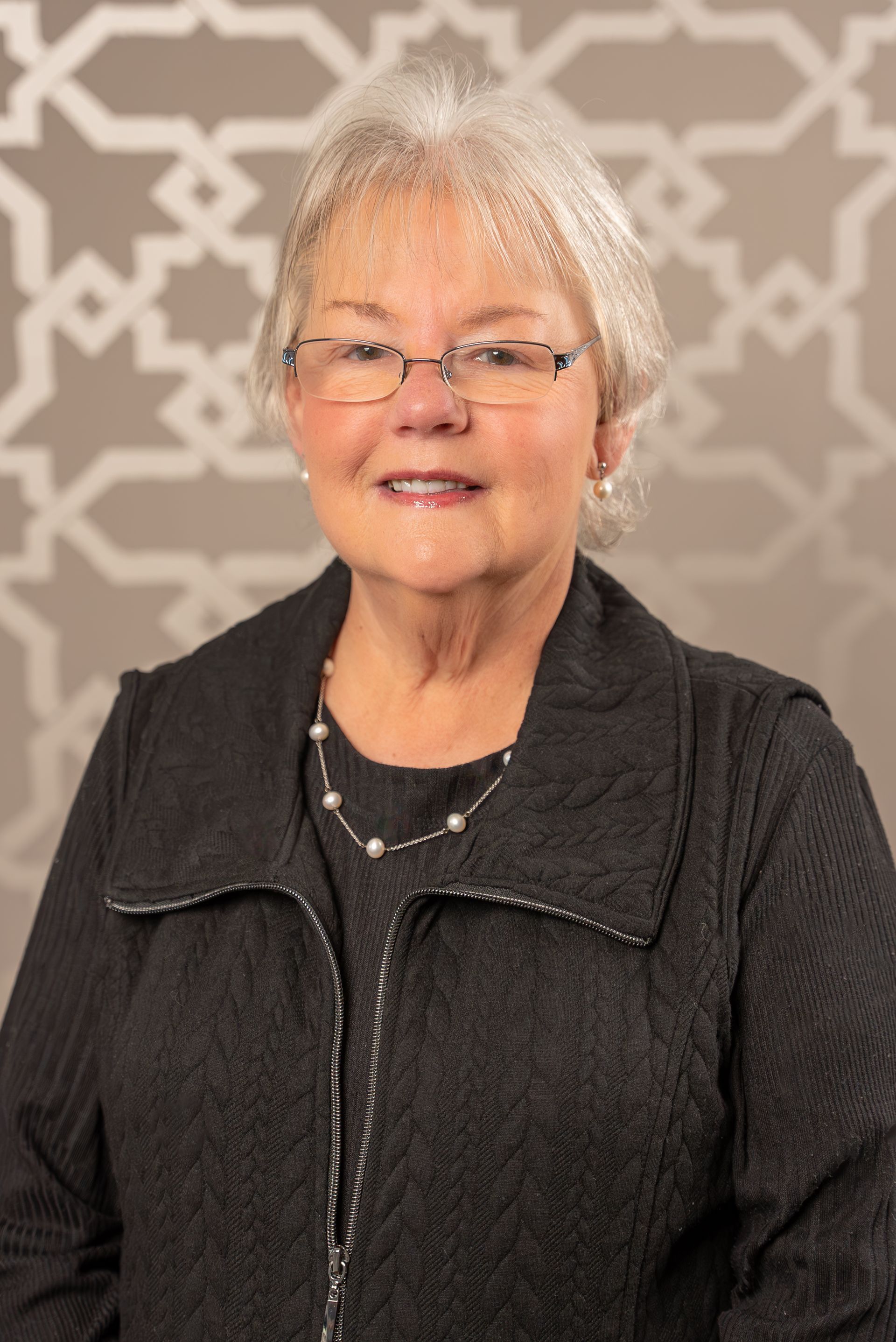 A woman wearing glasses and a black jacket is smiling for the camera.