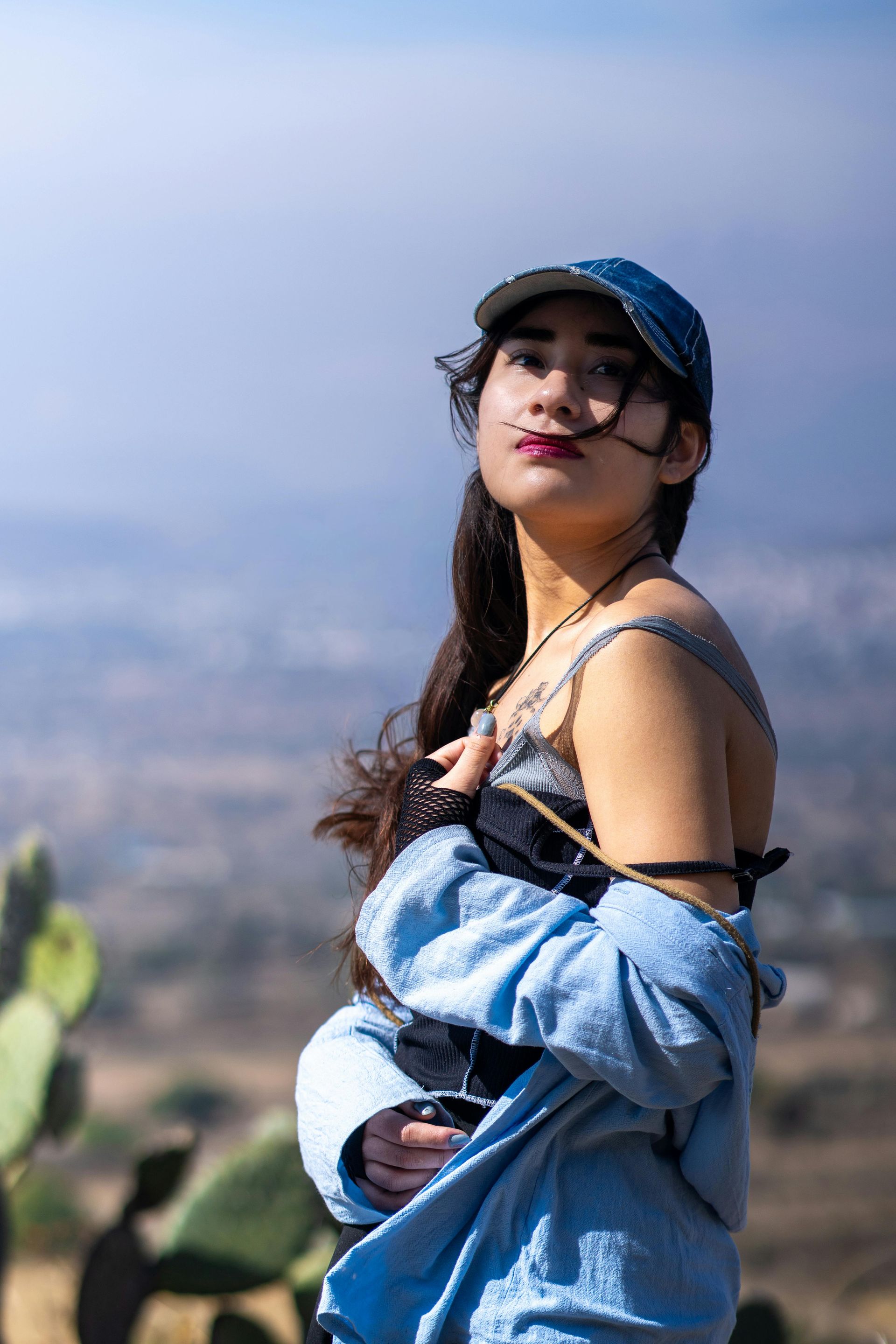 Woman with short dark hair, wearing a black tank top, looking over shoulder, outdoors, sunlit.