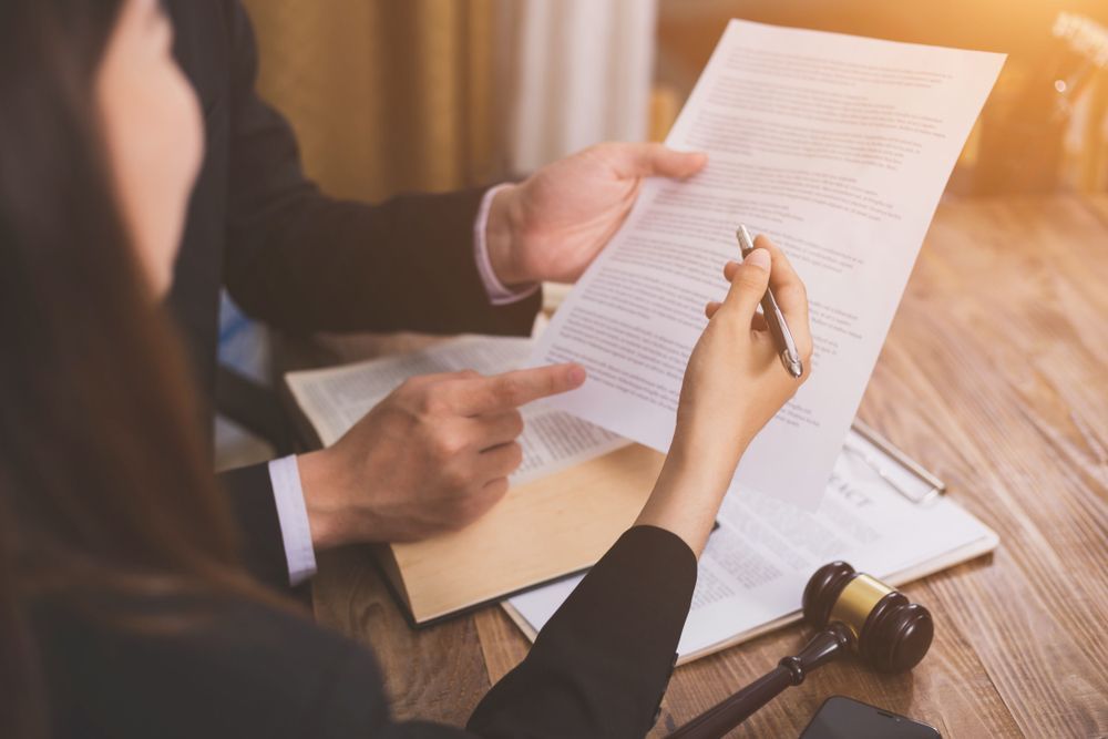 A Man And A Woman Are Sitting At A Table Looking At A Piece Of Paper — Queensland Lawyers Cairns In Cairns City, QLD