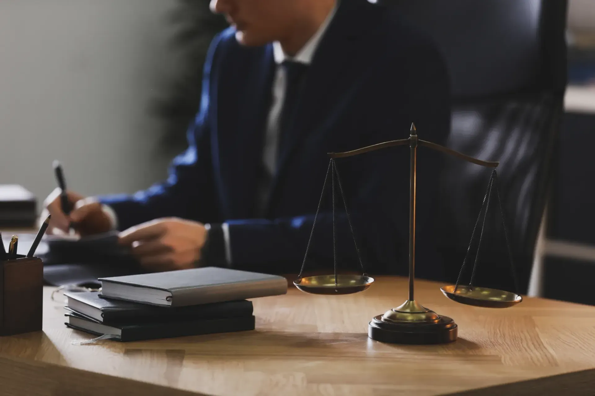 Lawyer Writing At Desk Beside A Scale Of Justice And Stacked Files - Queensland Lawyers in Cairns QLD