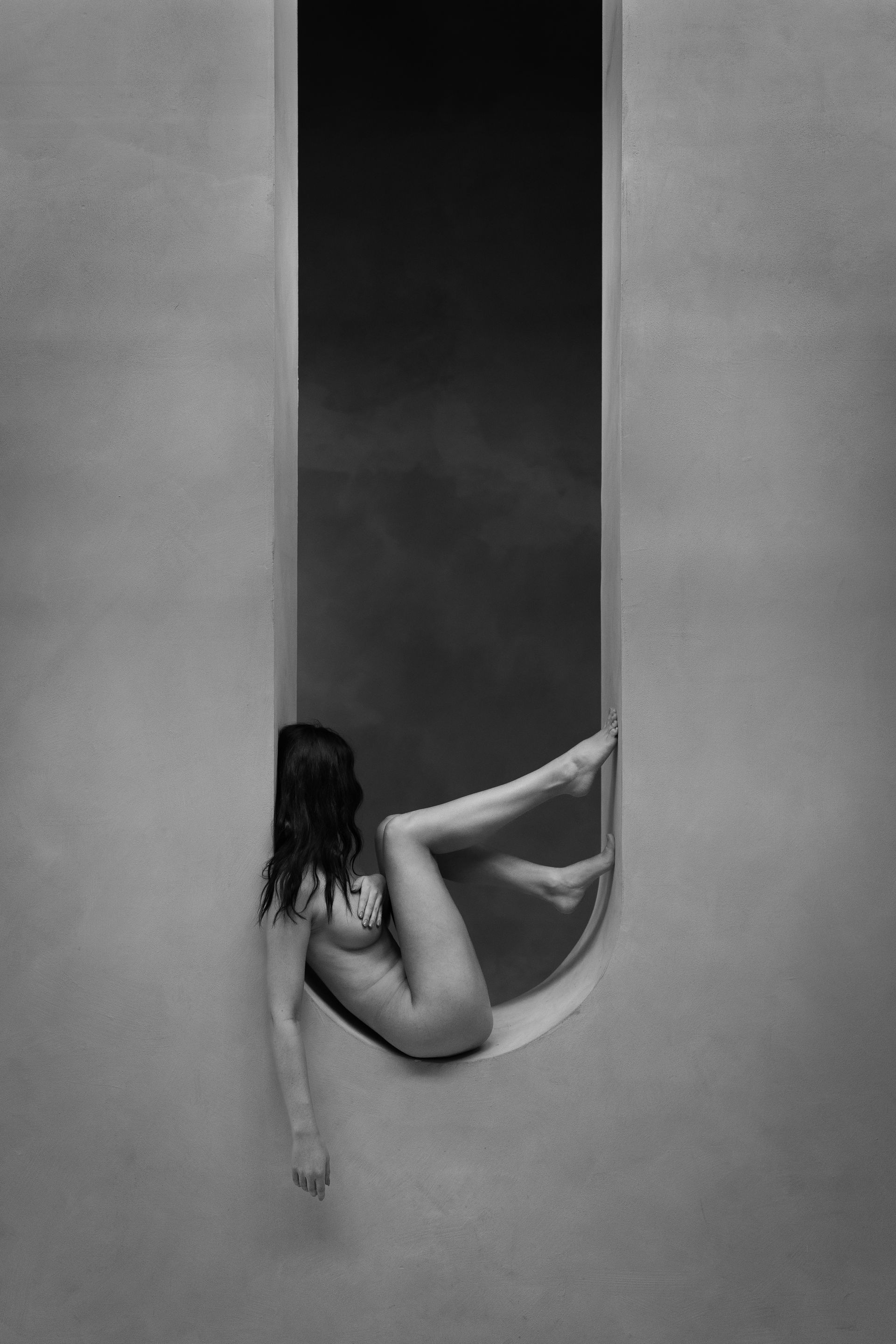 Vrouw in naaktpose, omlijst door een boogvormige opening. Zwart-wit.