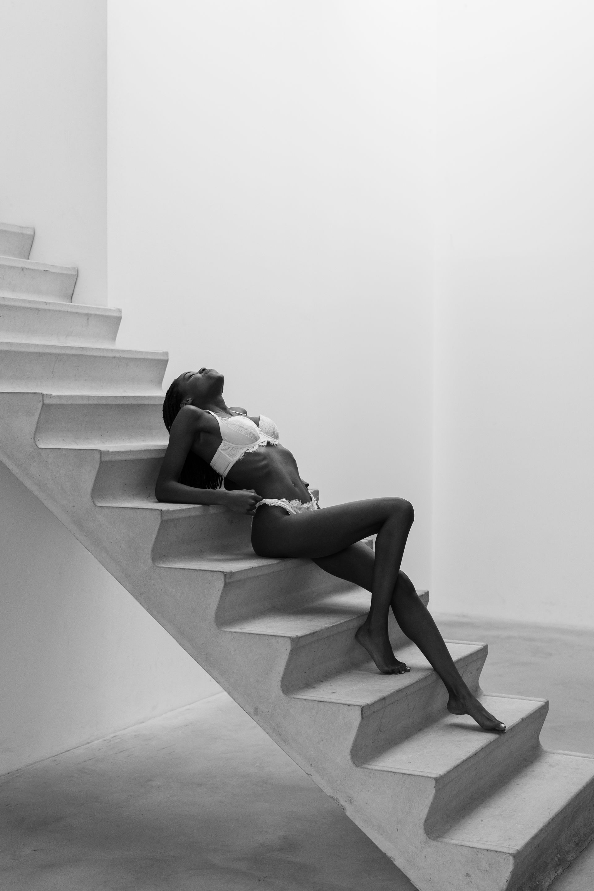 Vrouw liggend op een betonnen trap, in een zonovergoten interieur.