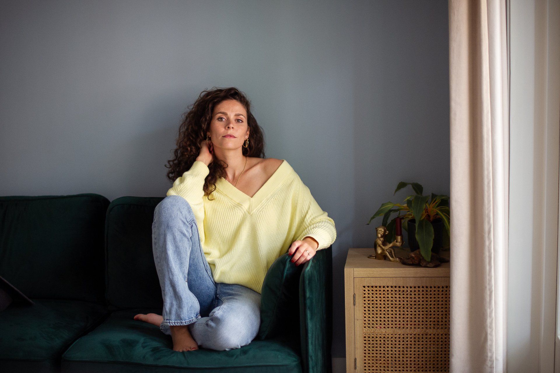 Een vrouw in een gele trui en spijkerbroek zit peinzend op een groene bank.