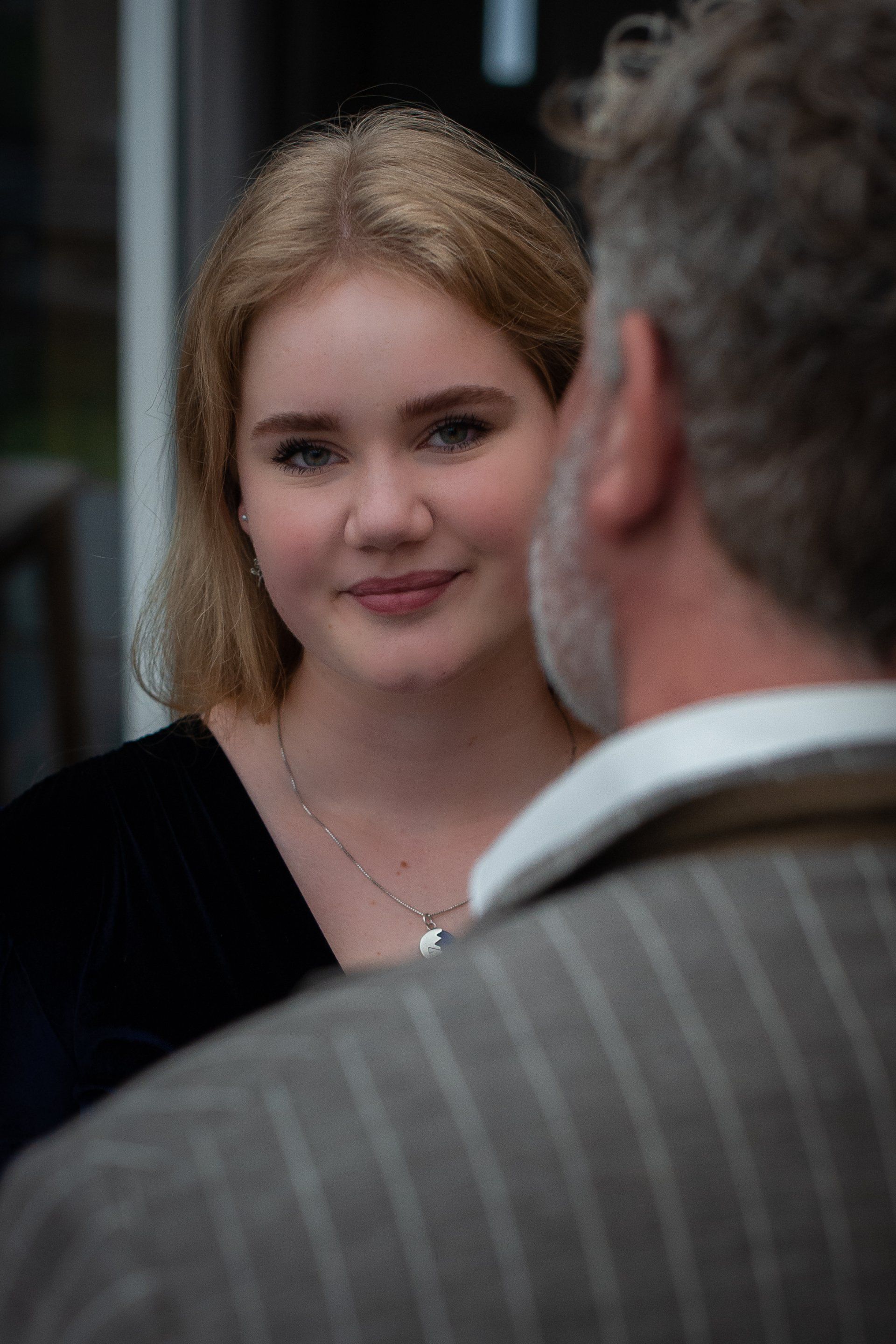 Een jong persoon lacht en kijkt naar iemand buiten beeld; zachte verlichting, binnenomgeving.