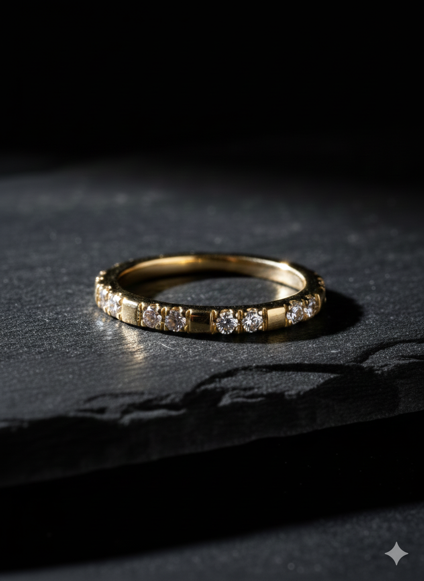 Gold band ring with small diamonds set on a dark slate surface.