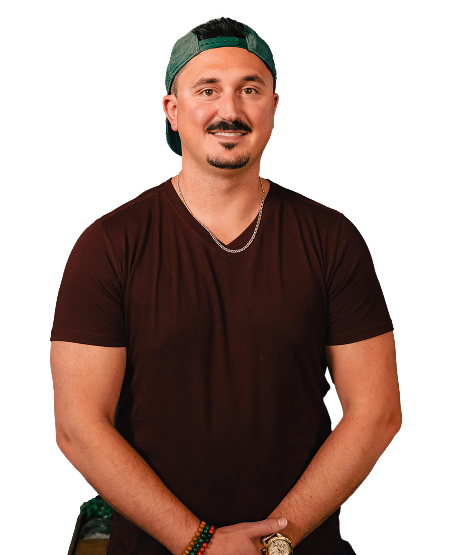 A man wearing a brown shirt and a green hat is standing with his arms crossed.