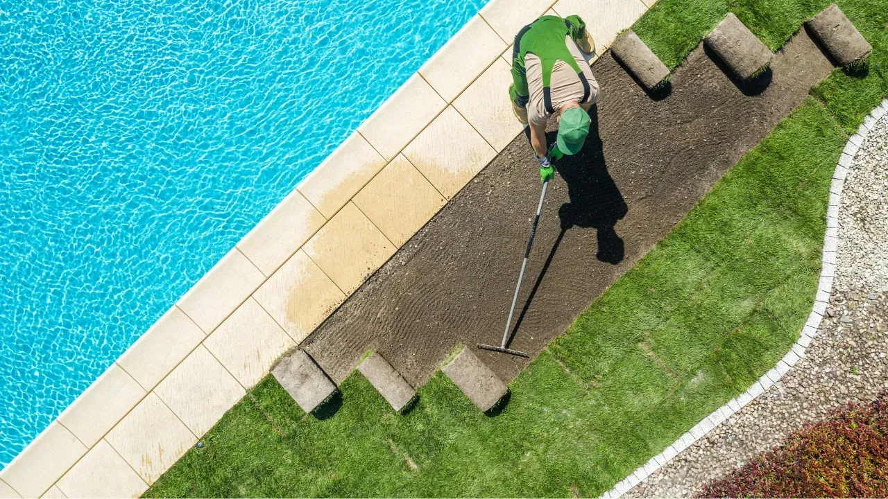 A worker laying sod near a pool patio