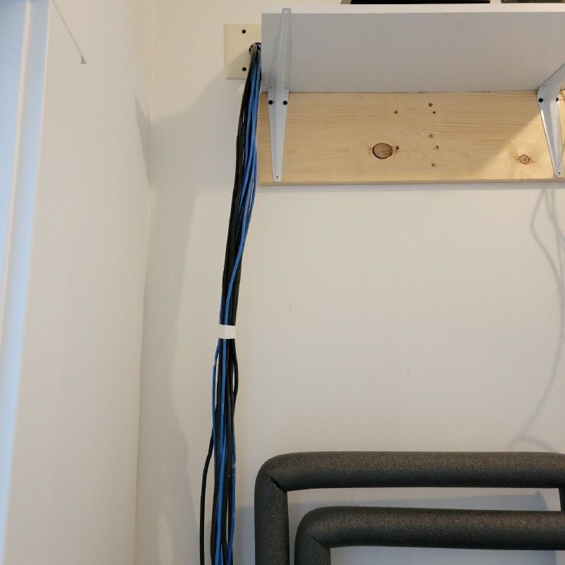 A bunch of wires are hanging from a wooden shelf