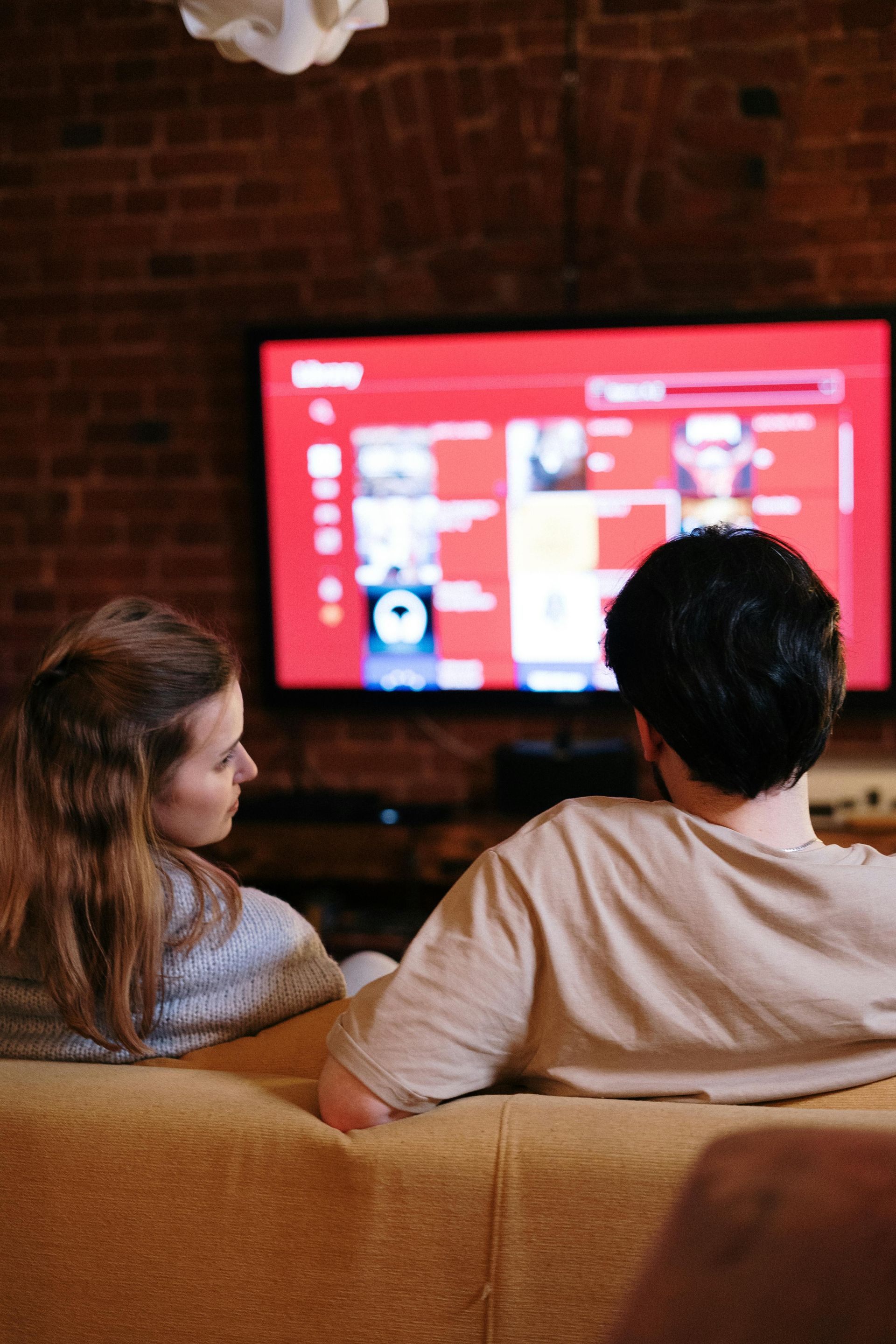 A man and a woman are sitting on a couch watching a television.