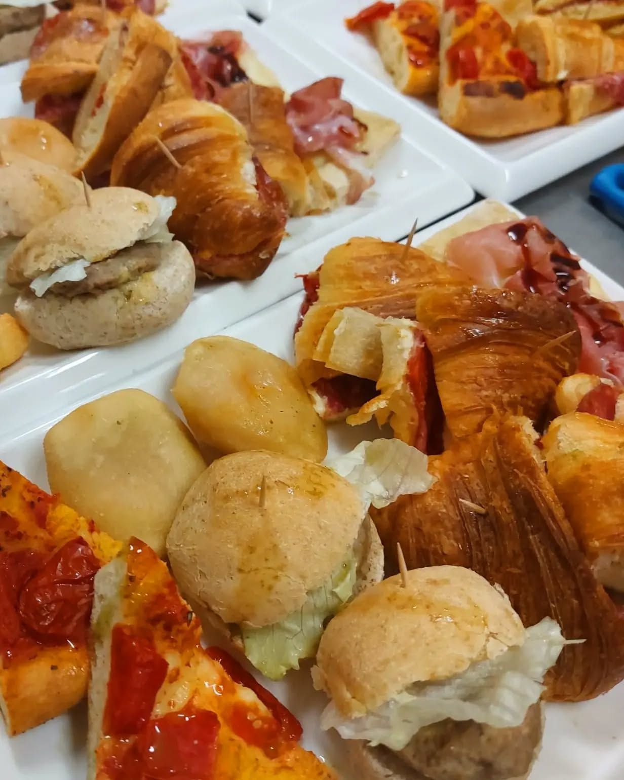 Piatti di antipasti assortiti: mini panini, croissant ripieni, mini pizze e bocconcini di patate.