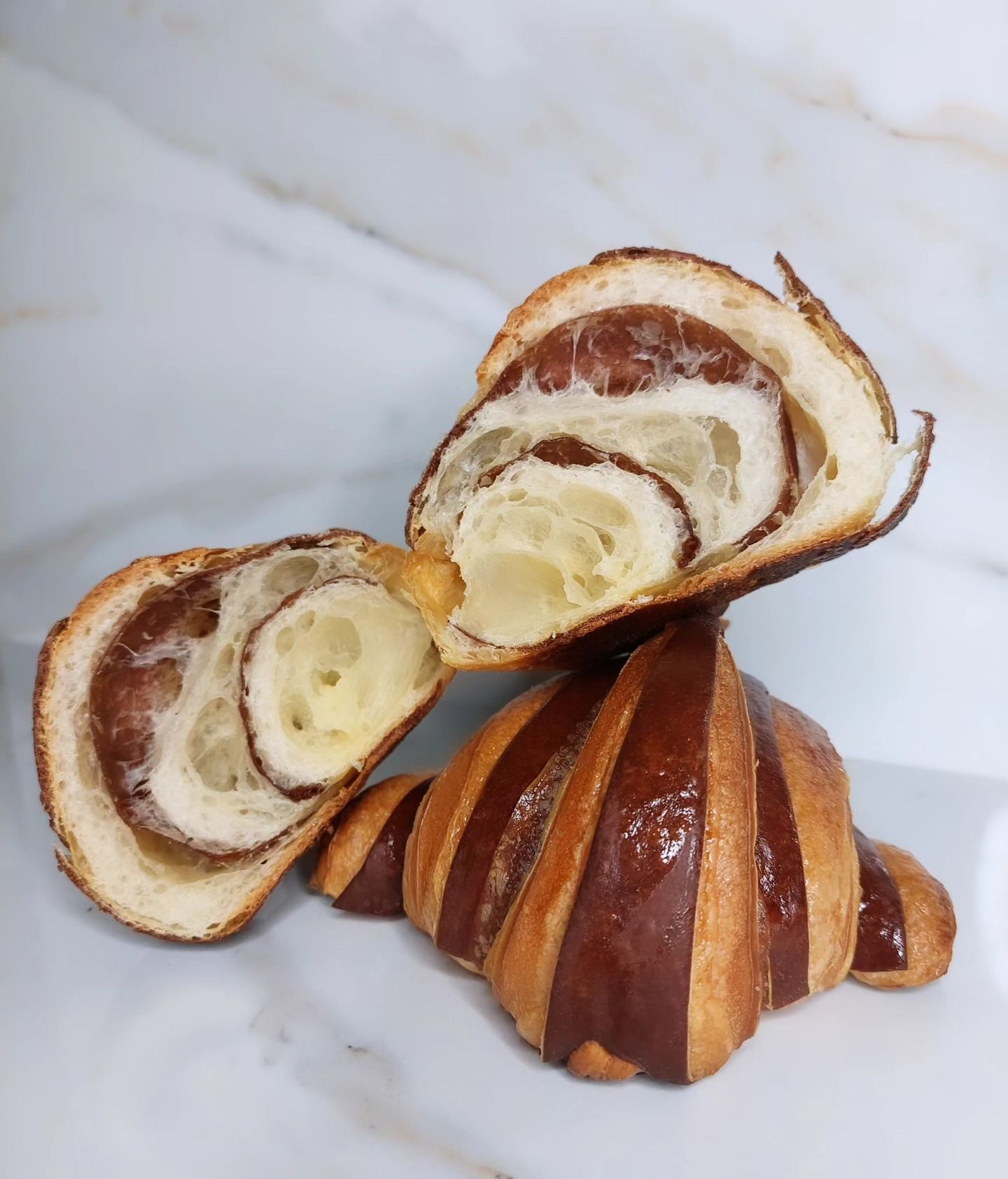 Croissant al cioccolato, tagliato a metà per mostrare gli strati, appoggiato su una superficie bianca.