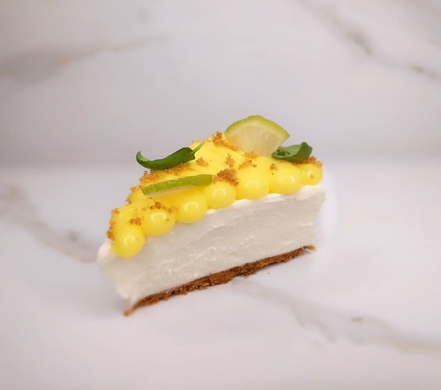 Fetta di cheesecake al limone su una superficie di marmo, guarnita con crema gialla e fette di limone.