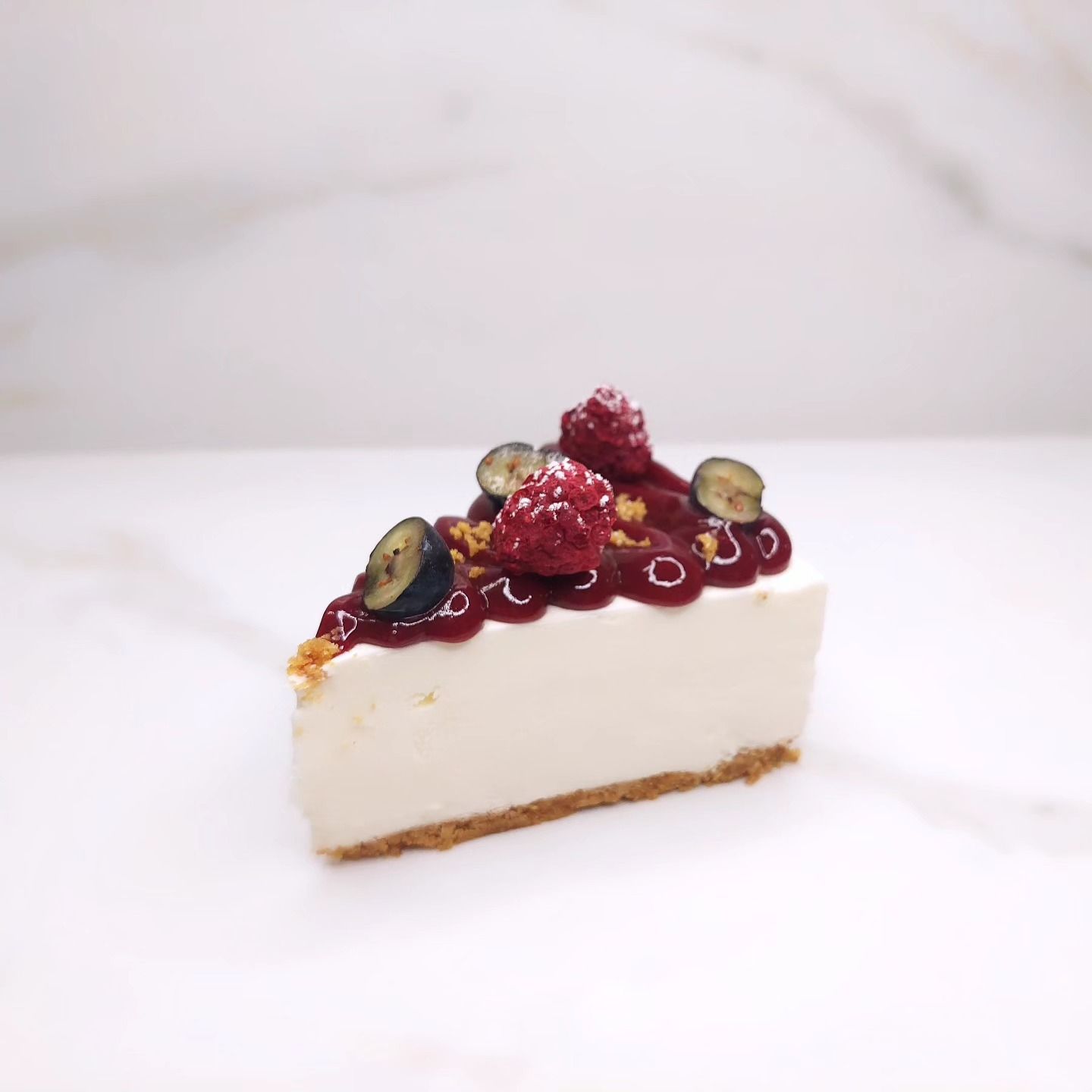 Fetta di cheesecake con guarnizione di composta di frutti di bosco e frutti di bosco freschi su una superficie bianca.