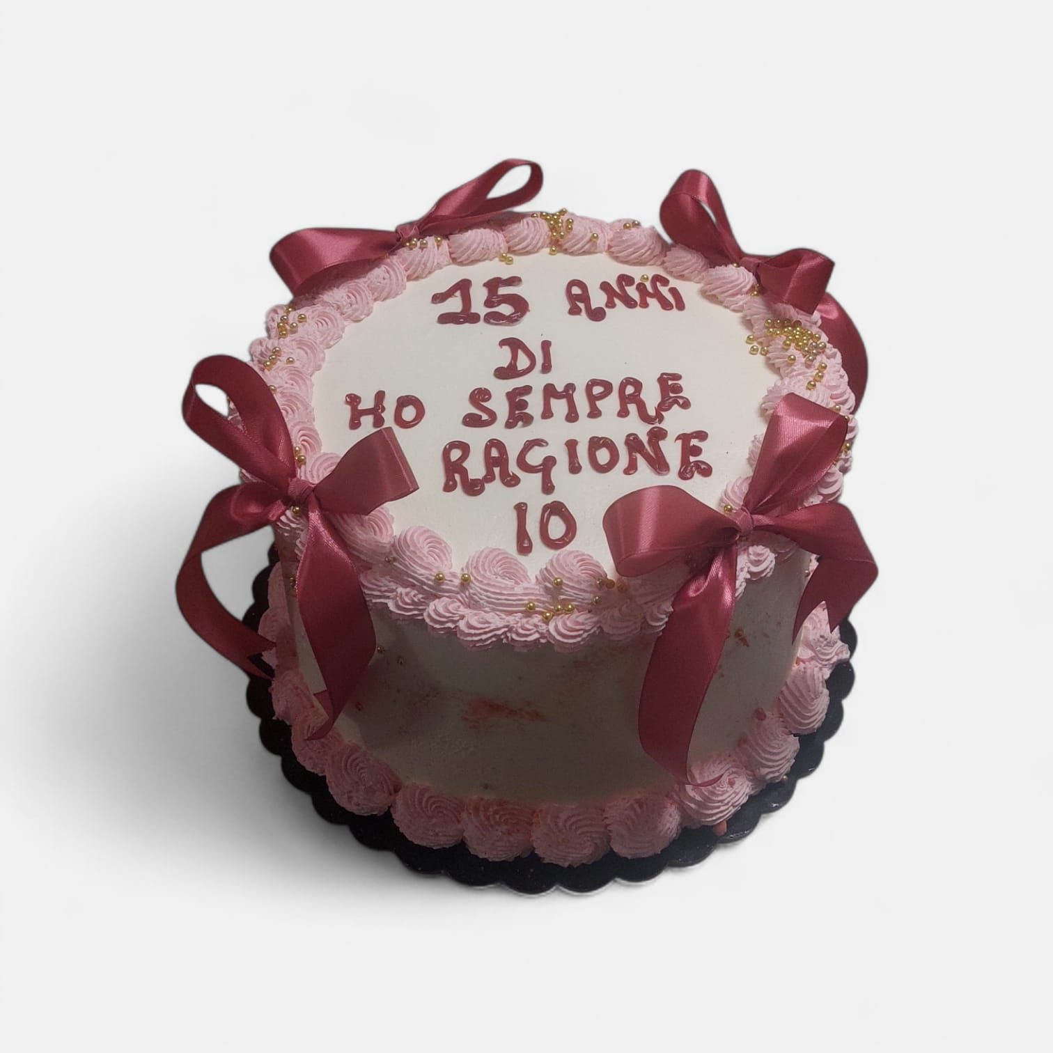 Torta con glassa rosa, fiocchi rosso scuro e la scritta 