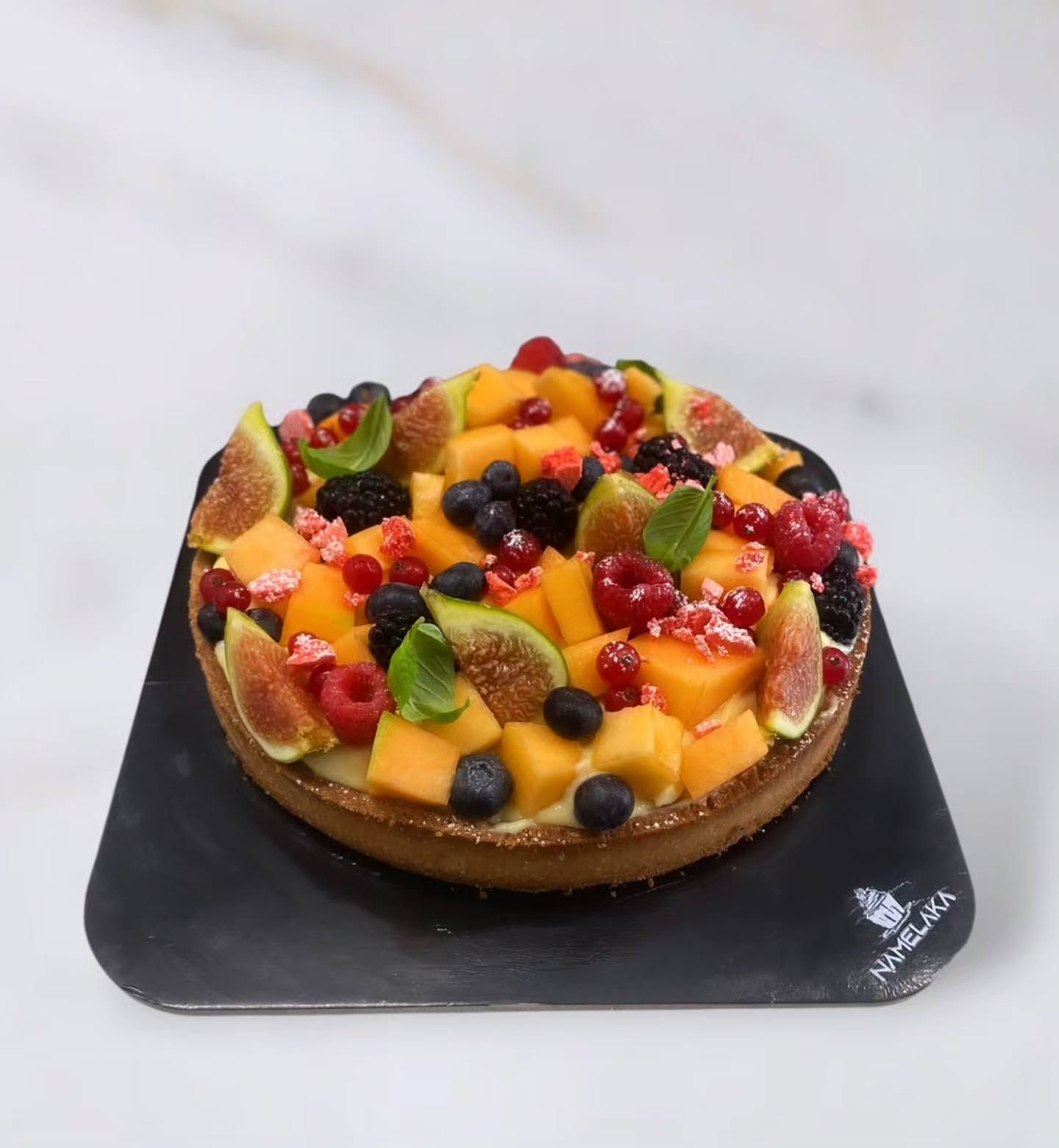 Crostata di frutta con vari frutti colorati su una base scura.