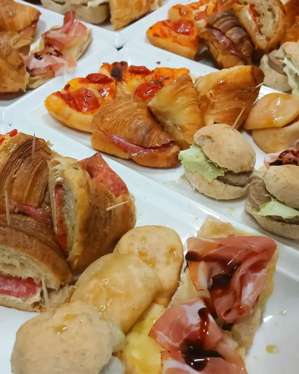 Piatti di antipasti assortiti: mini pizze, panini, croissant e pasta fritta.