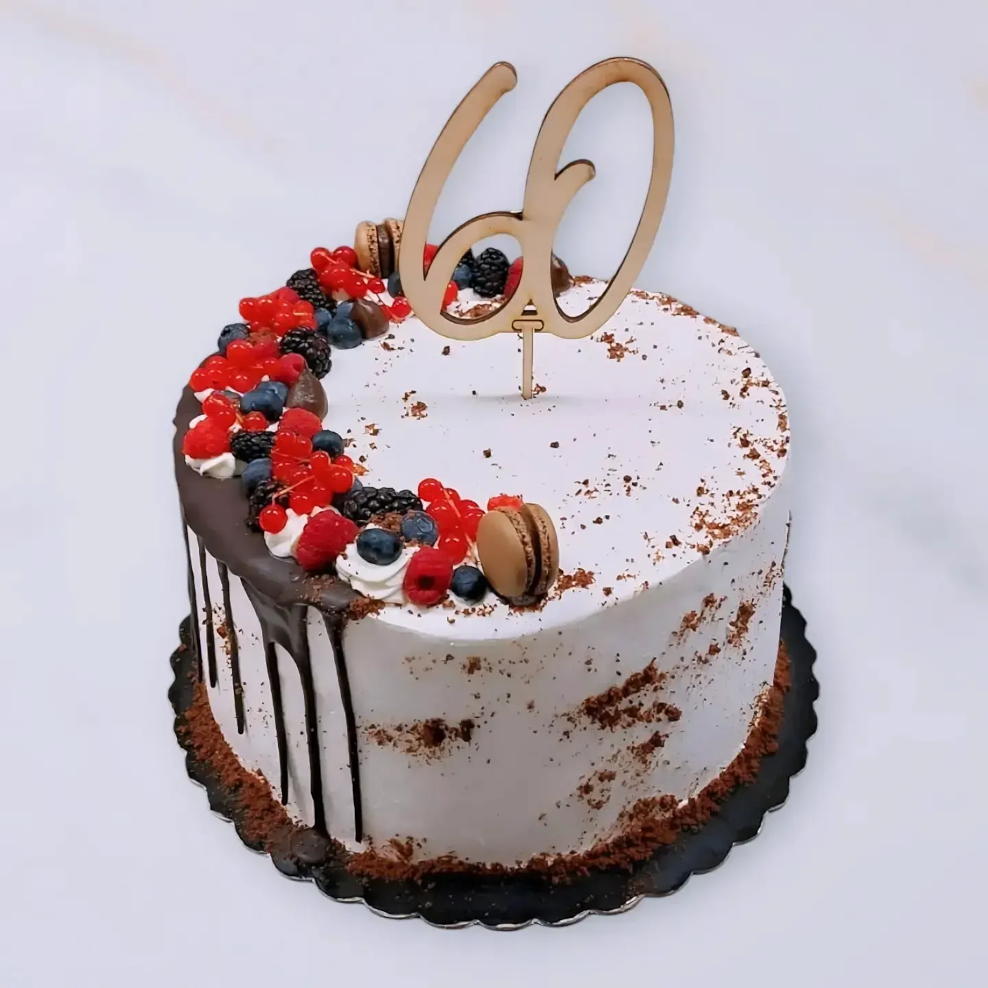 Torta con glassa bianca, gocce di cioccolato, frutti di bosco, macarons e una decorazione con la scritta