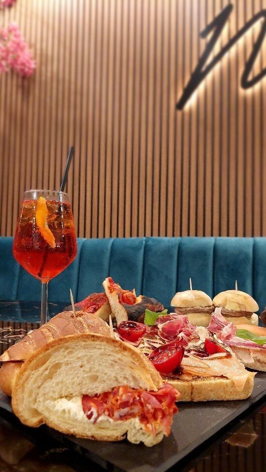 Antipasti e un cocktail su un tavolo in un ristorante, con una parete in legno e una panca blu come sfondo.