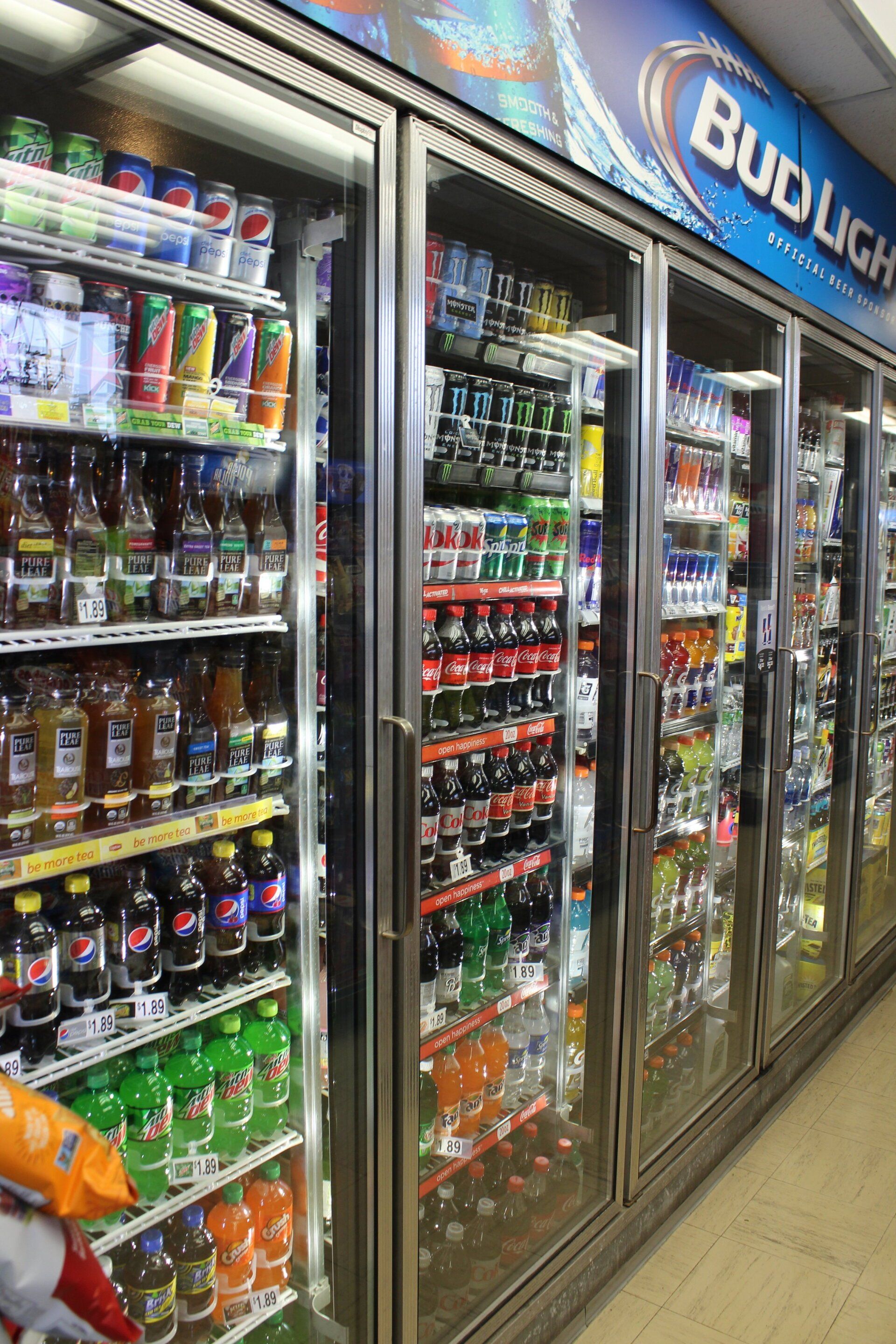 A bud light sign hangs above a refrigerated section of a store