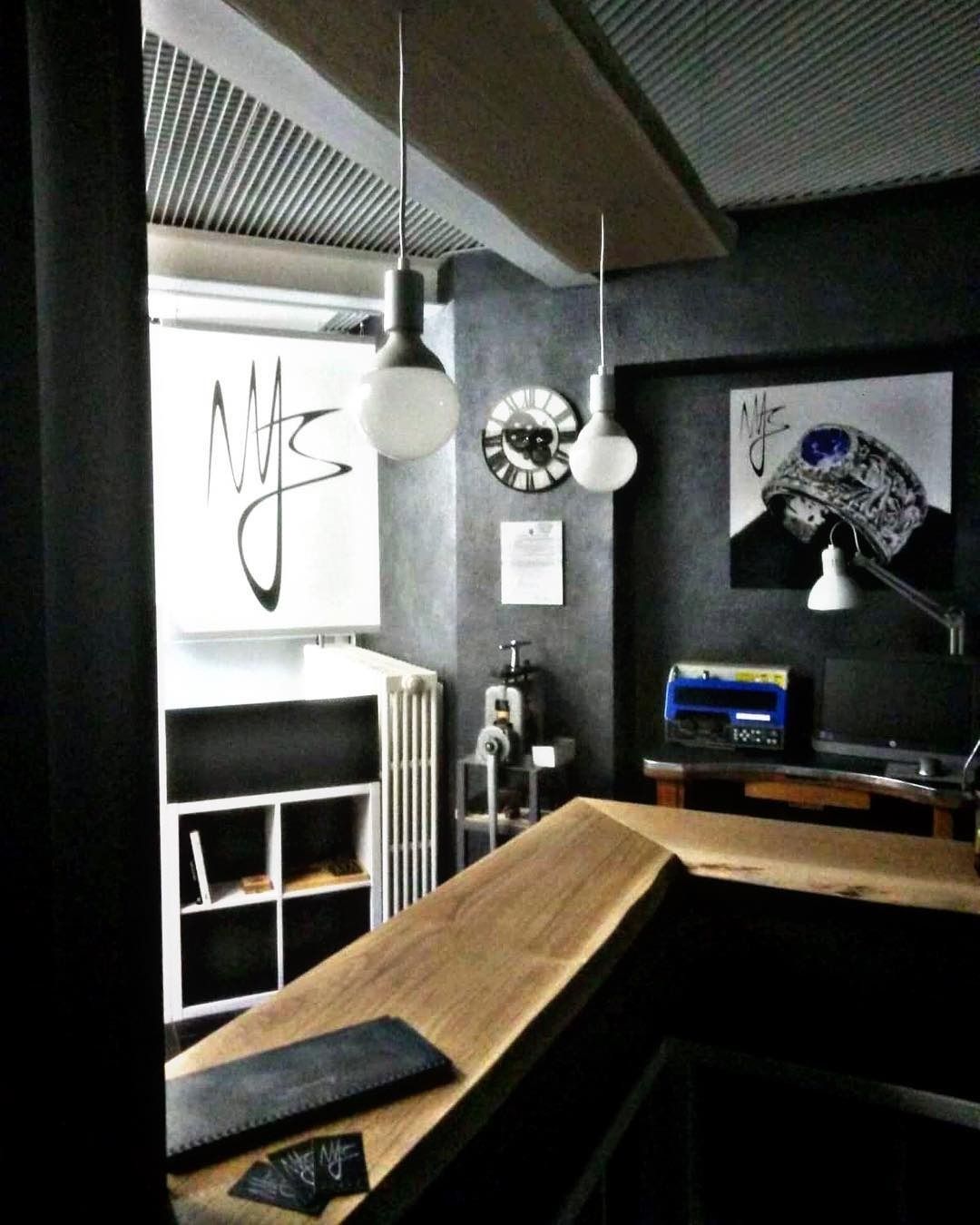 Interno di uno spazio moderno con opere d'arte e un bancone in legno, illuminato da luci sospese, pareti scure.