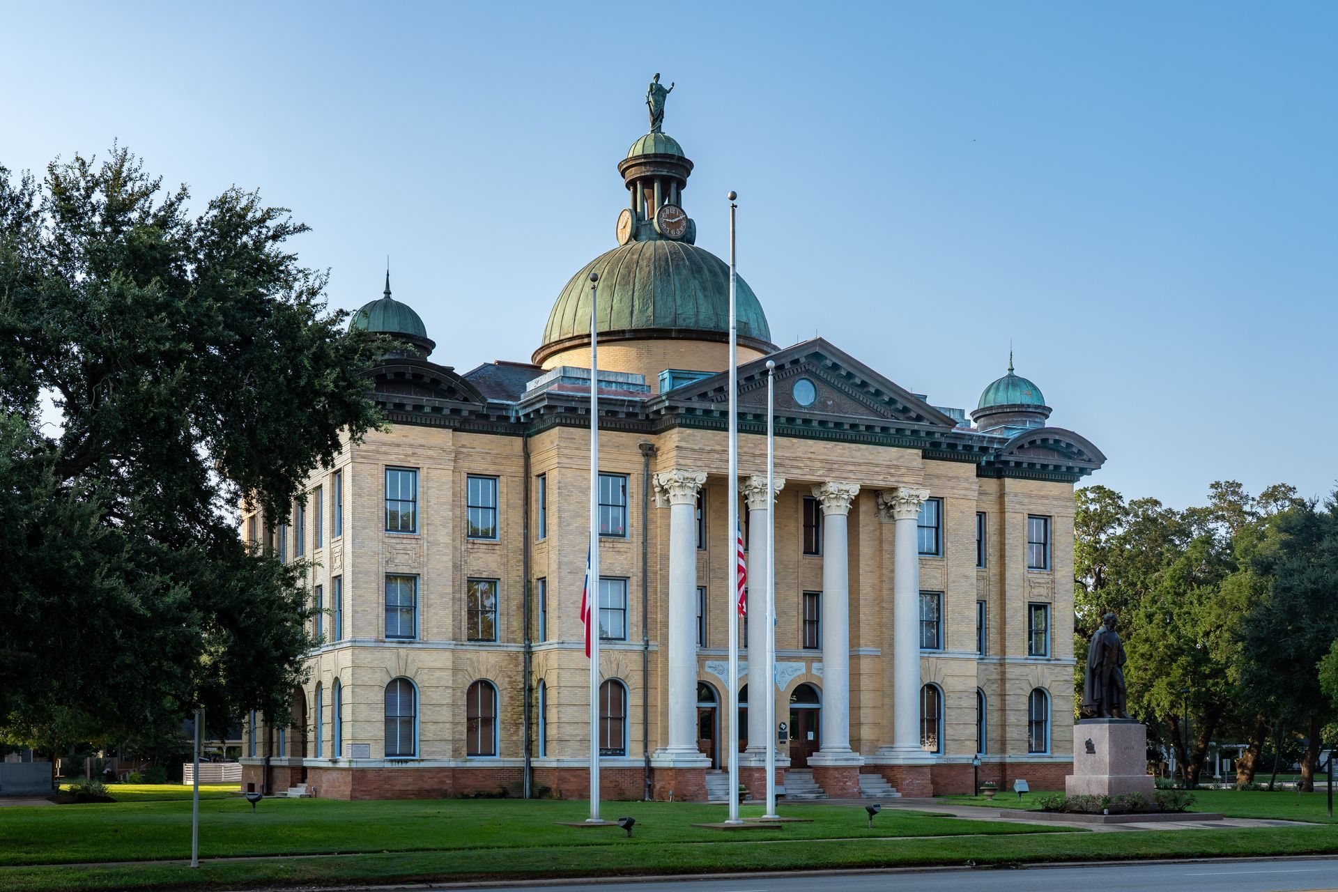 Beige brick courthouse with copper dome and columns, green lawn, clear sky.