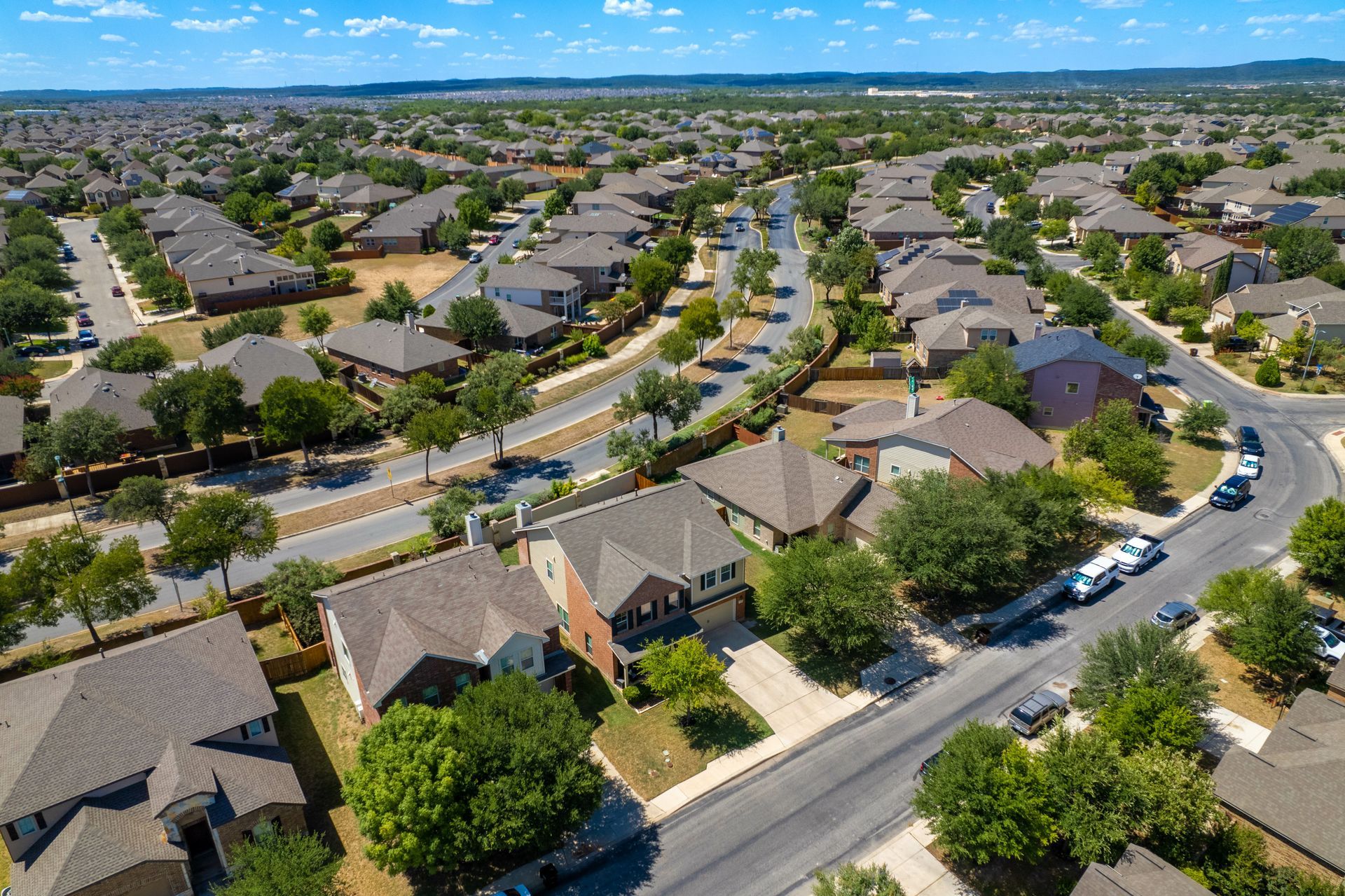 Aerial view of suburban houses with brown roofs, trees, and roads.