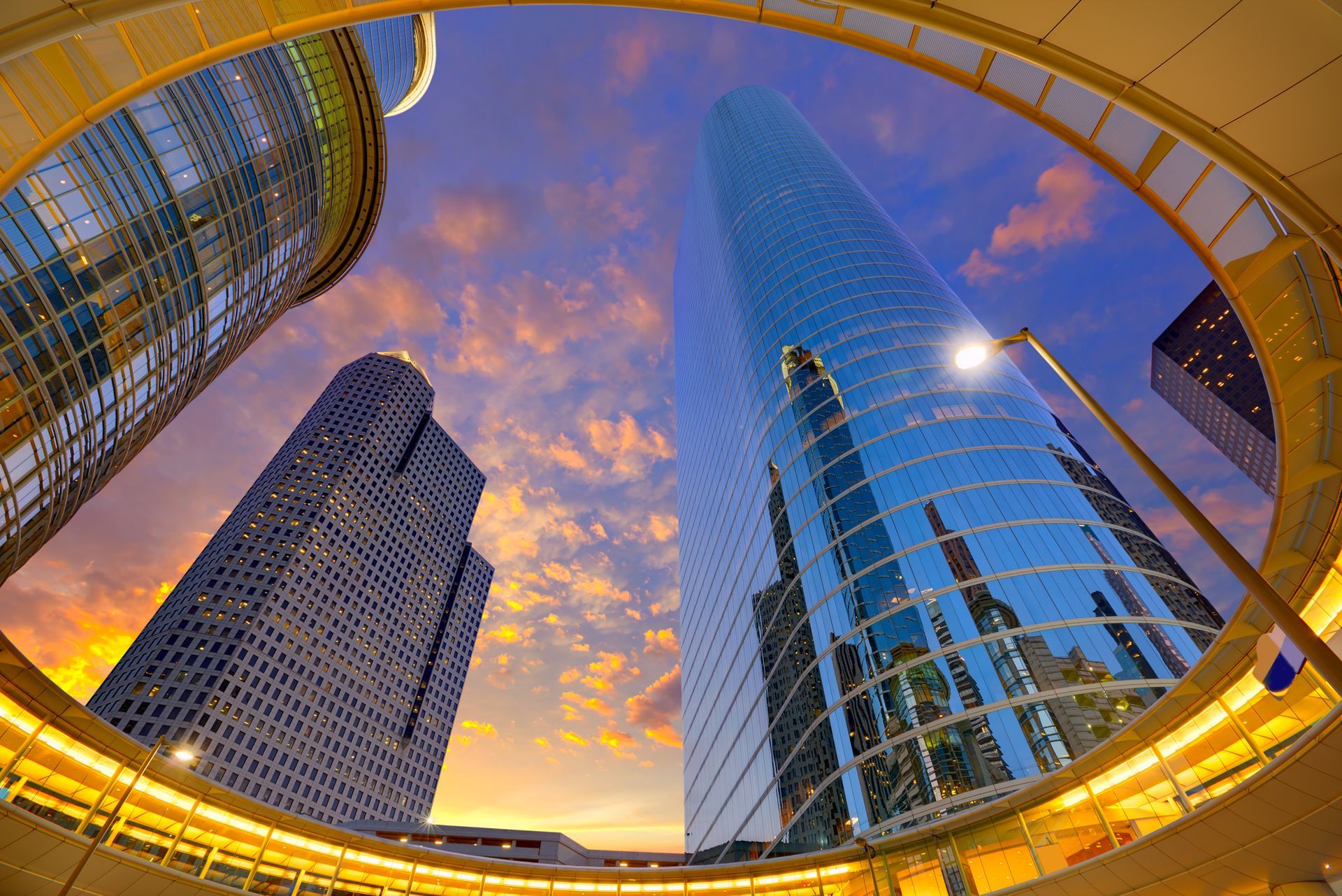 Skyscrapers against a colorful sunset, viewed from a circular structure, in an urban setting.