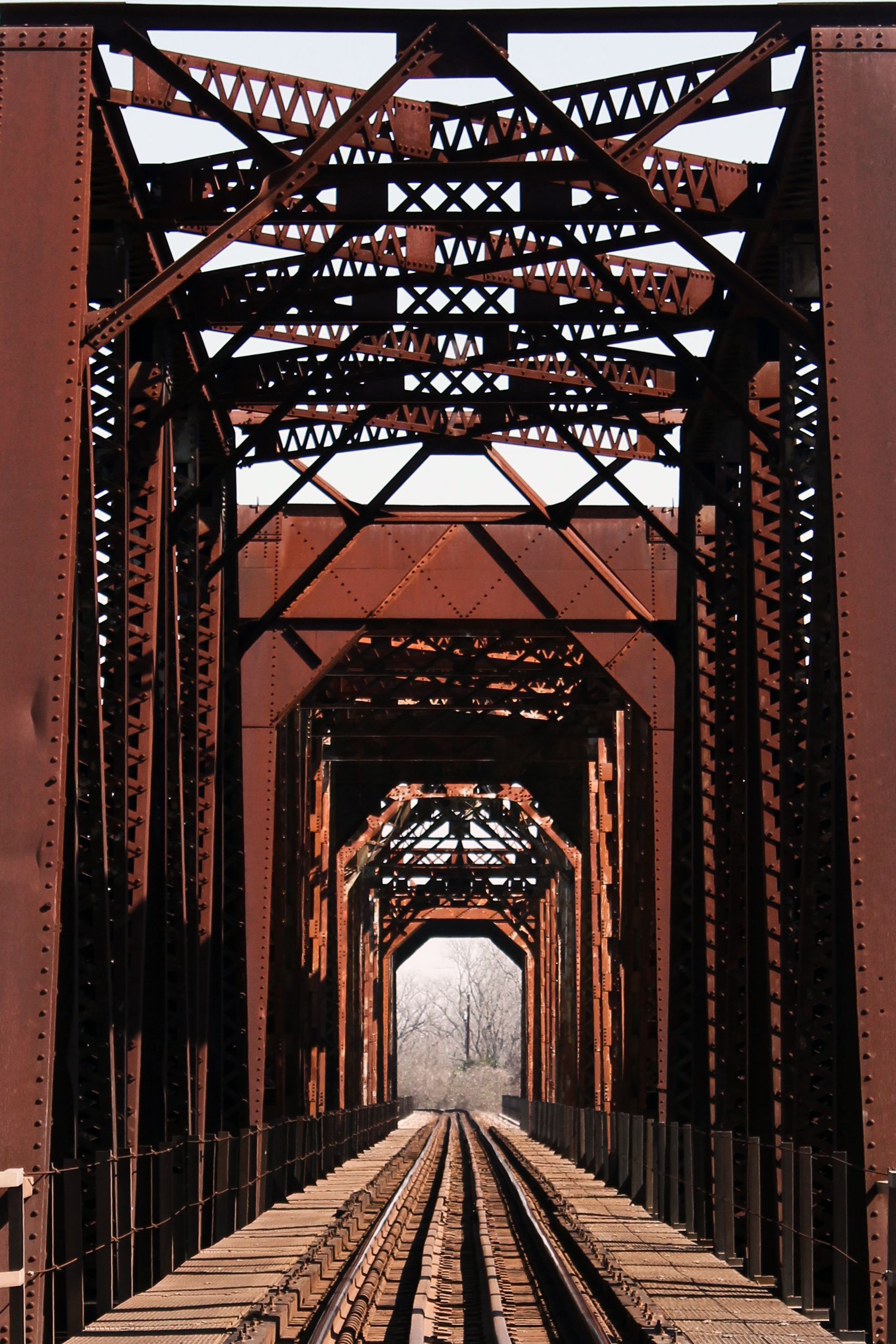 Rusty steel railroad bridge with tracks leading into the distance.