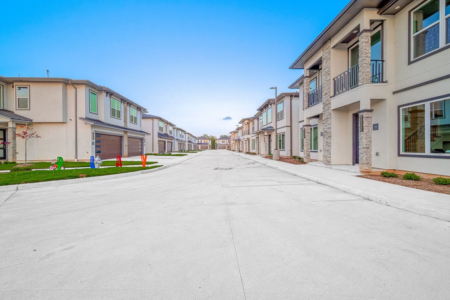 Row of modern townhouses lining a wide, empty residential street under a clear blue sky