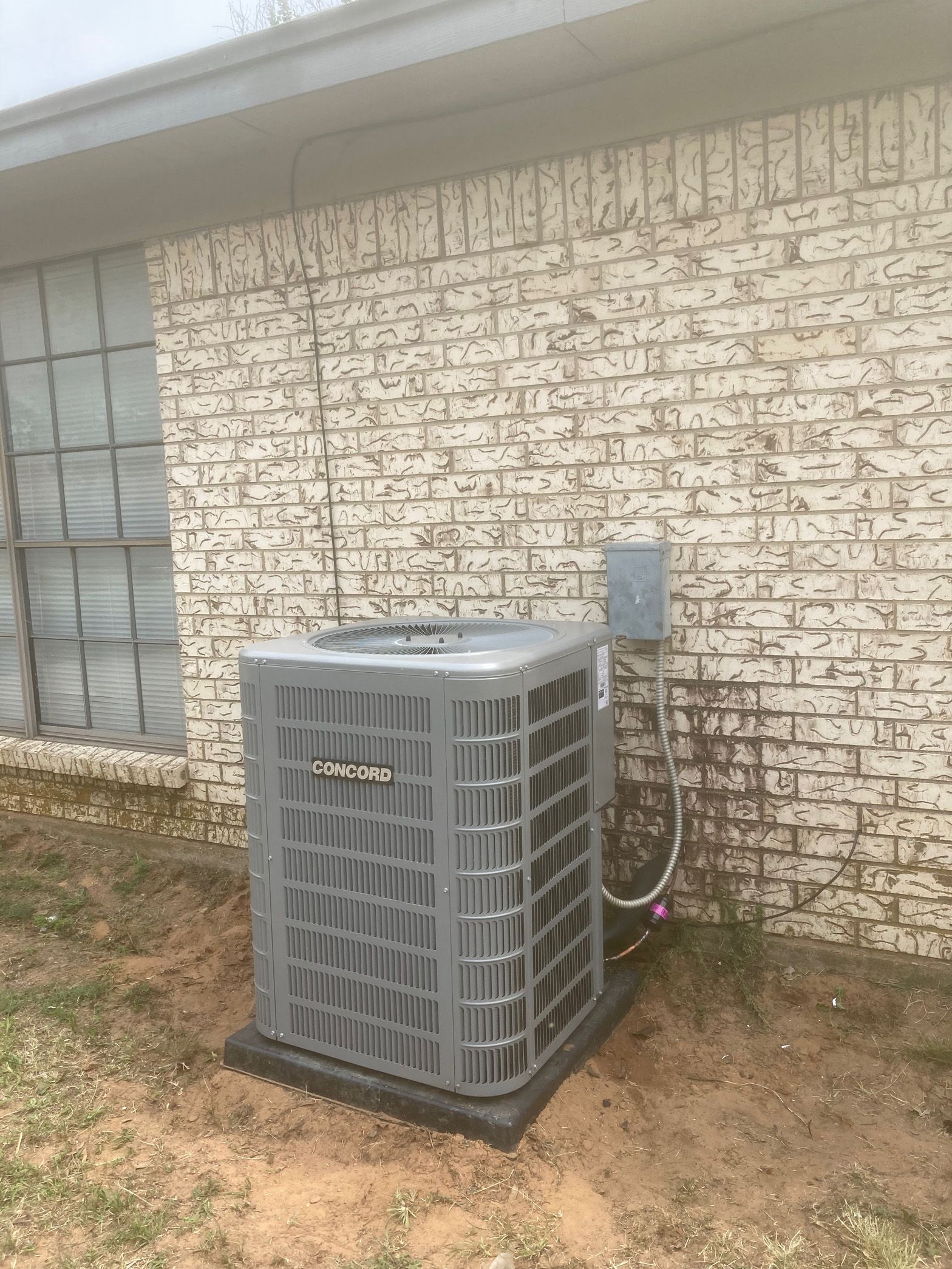 An air conditioner is sitting on the side of a brick building.