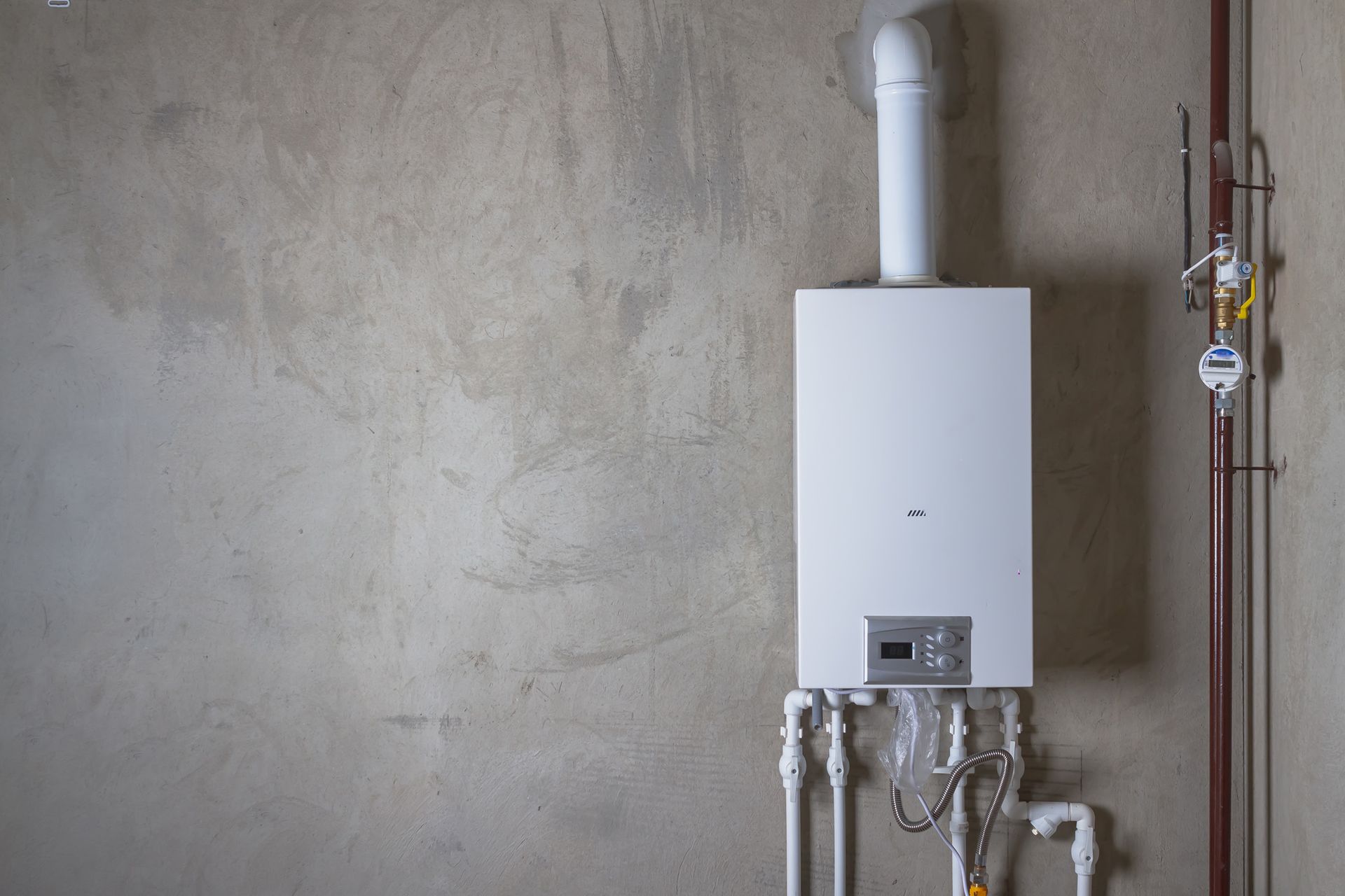 A white boiler is hanging on a wall next to pipes.