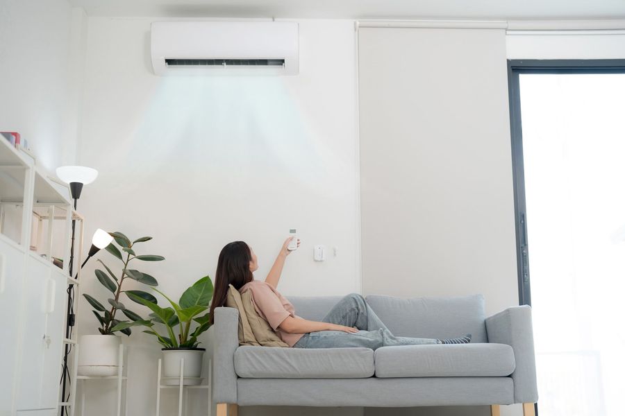 A woman is laying on a couch in a living room using an air conditioner.