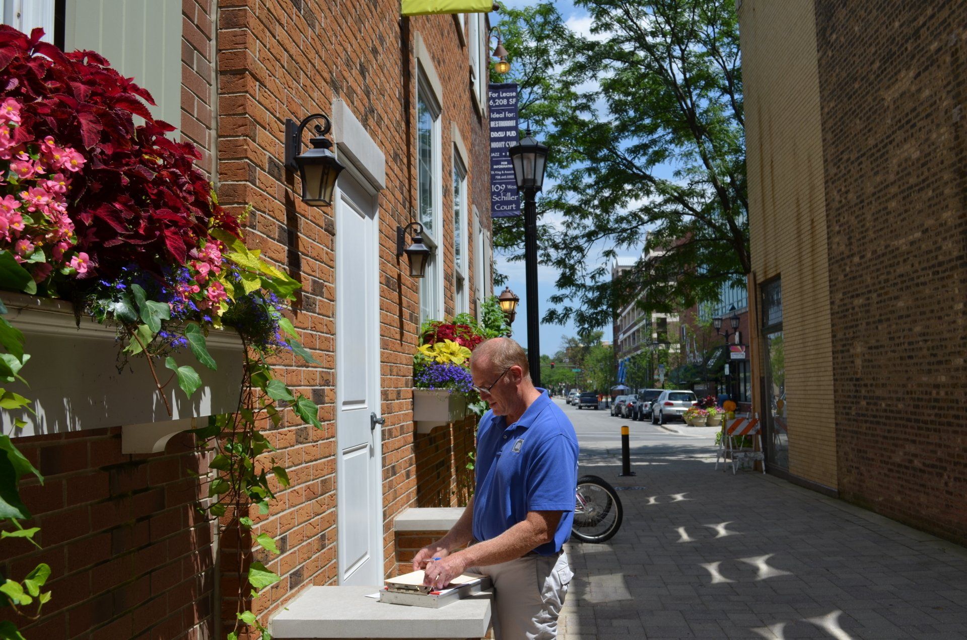 A man in a blue shirt is standing on a sidewalk in front of a brick building.