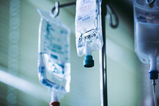 A couple of bags of iv fluid hanging from a pole in a hospital room.
