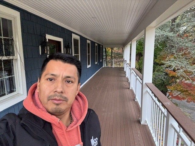 Two men installing a wooden mantel on a brick fireplace in a room with white walls.