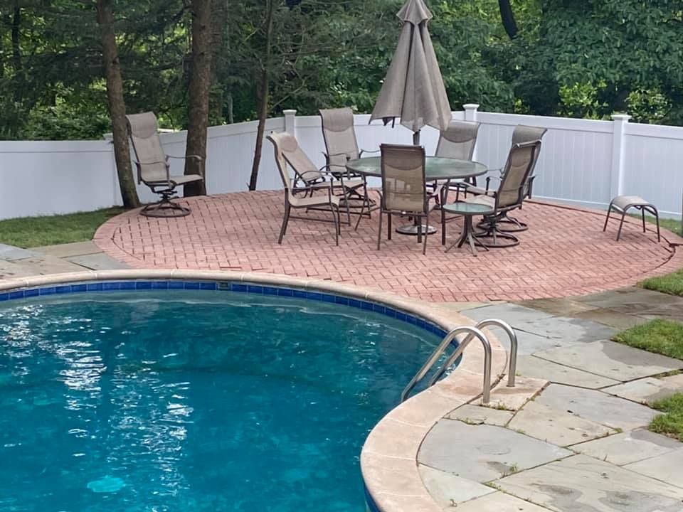Round pool with patio, dining set, and umbrella, enclosed by a white fence.